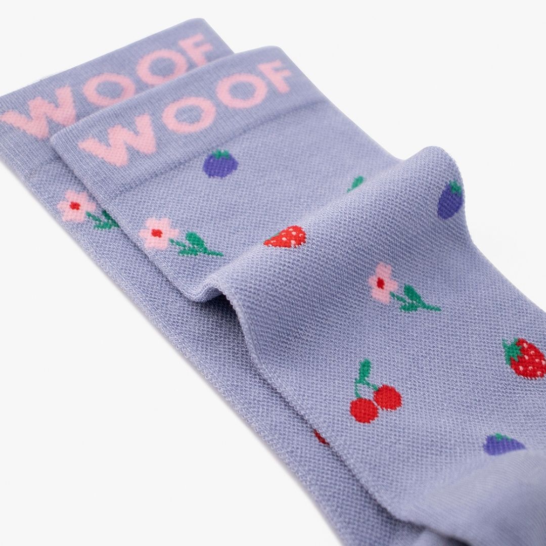 A Cherries & Berries Bamboo Crew Compression Socks folded neatly to highlight the pink woven "WOOF" cuff bands and the fruit-and-floral knit pattern layout.